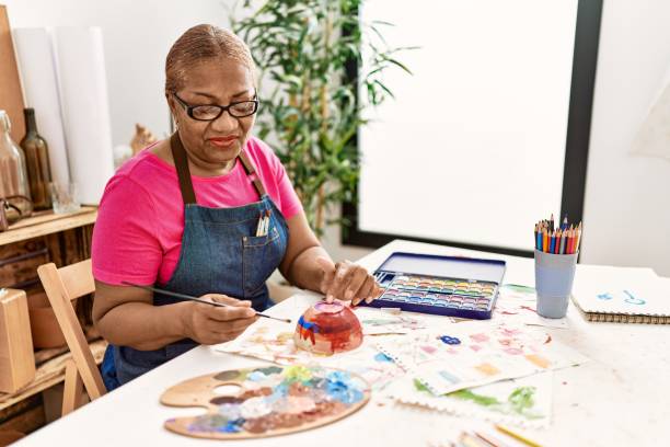 A senior woman painting ceramics by a sunlit window